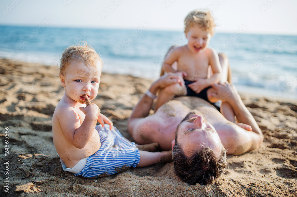 A father with two toddler children lying on sand beach on summer holiday. A father with two toddler children lying on sand beach on summer holiday.