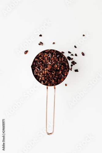 Rose gold measuring cups of cocao nips on a white background, healthy food concept