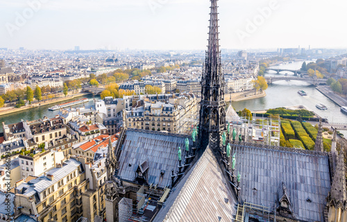 View from the tower of Notre-Dame de Paris over the ile de la Cite and the Seine with the rooftop and spire of the cathedral in the foreground and tour boats cruising on the river by a misty morning.