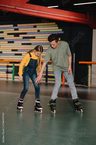 Handsome young instructor showing skating technics to attentive child
