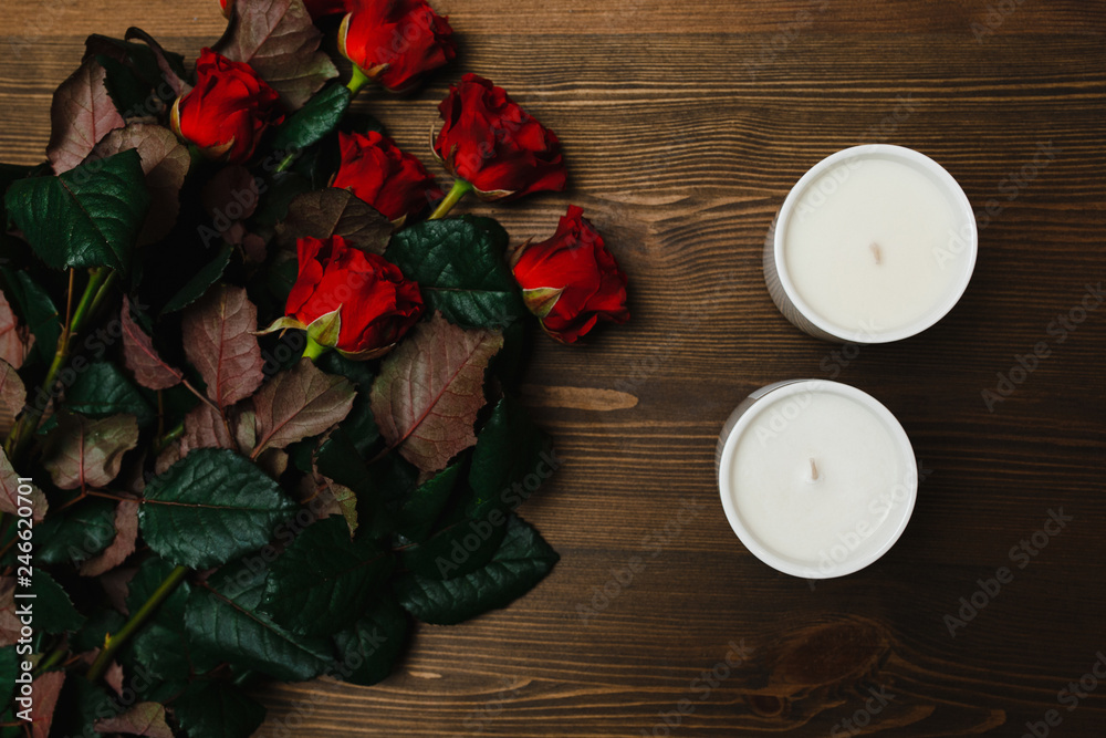 Red roses and white candles on the wooden surface Red roses and white candles on the wooden surface