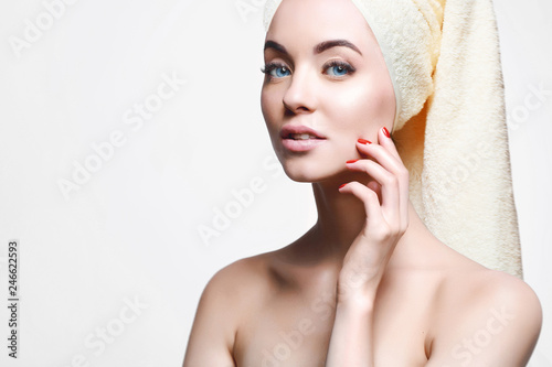 Woman applying moisturizer cream on her face. Portrait of young beautiful girl with healthy glow perfect smooth skin with towel on head. Cosmetology, beauty, skincare concept. Gray background.