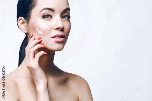 Woman applying moisturizer cream on her face. Portrait of young beautiful girl with healthy glow perfect smooth skin. Cosmetology, beauty, skincare, skin, facial cosmetic concept. Gray backgrond.