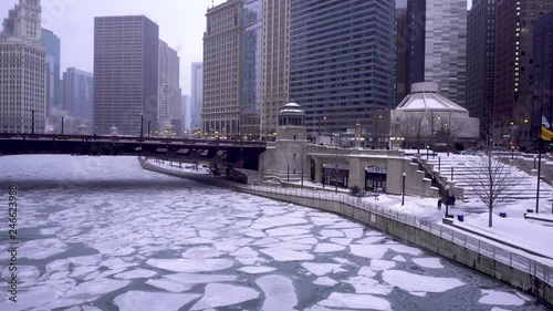 view from the Chicago river during the cold winter months.  the river is completely frozen while few people venture around downtown