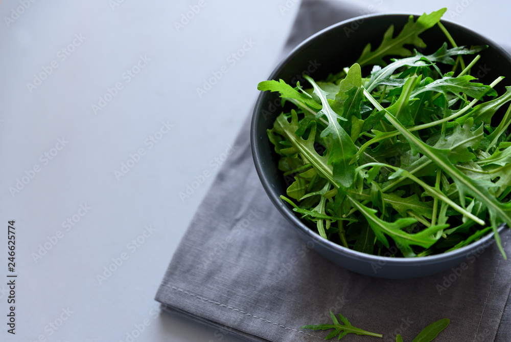 Fresh green arugula in bowl on gray wooden background. Healthy food or vegetarian concept. Top view. Copy space Fresh green arugula in bowl on gray wooden background. Healthy food or vegetarian concept. Top view. Copy space