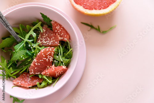 Fresh citrus salad with arugula, grapefruit and sesame seeds on pink background. Selective focus. Raw vegetarian spring detox food.