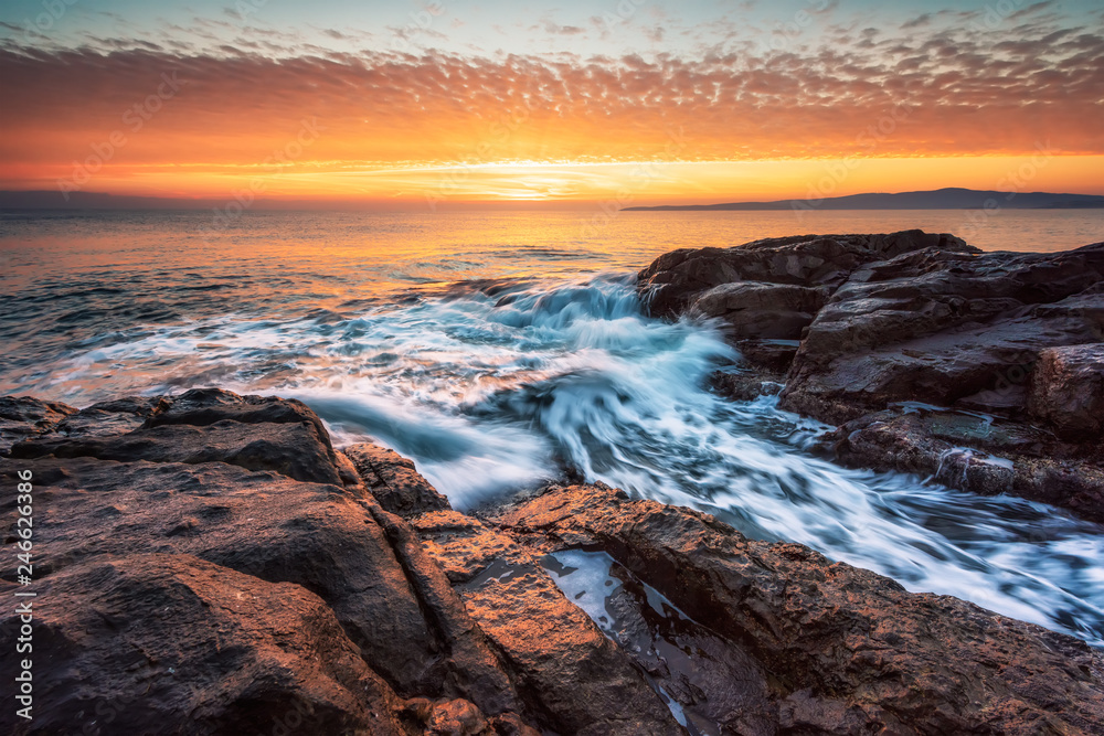 Obraz premium Stormy sea with colorful sunrise sky at the rocky coastline of the Black Sea