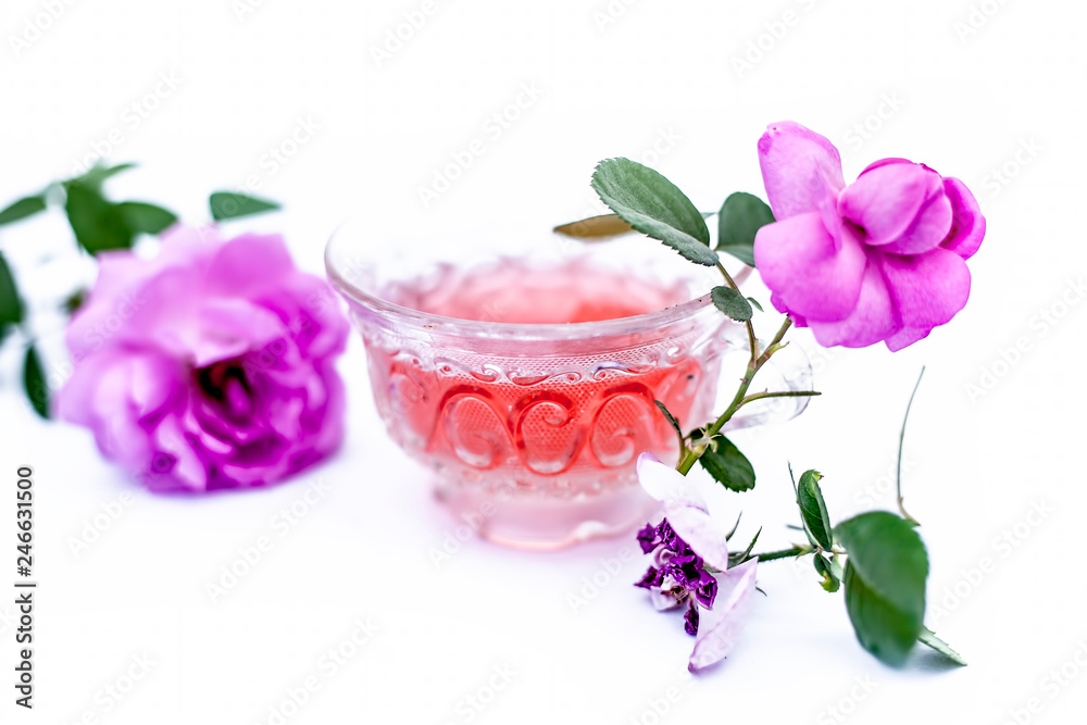 Close up view of organic fresh rose tea in a transparent glass cup isolated on white with raw roses.