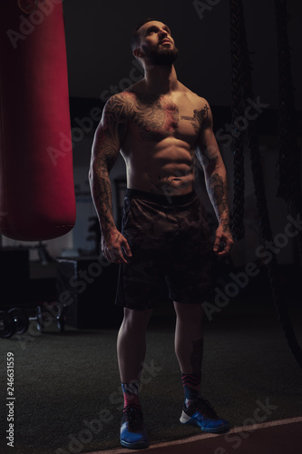 Shirtless tattooed athlete looking up by the heavy bag