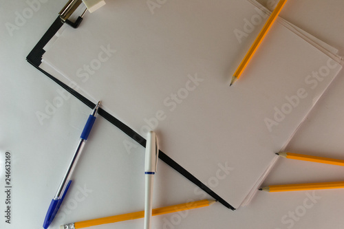 Black tablet with office paper around which pens and pencils are scattered
