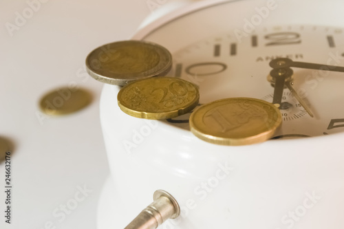 Three gold coins of different denomination lie on the glass of the alarm clock close-up photo