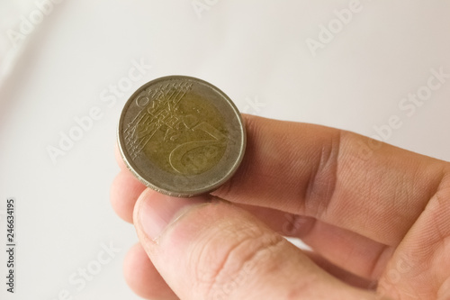 Coin of two euros in close-up shot on a white background lies on the thumb of the right hand