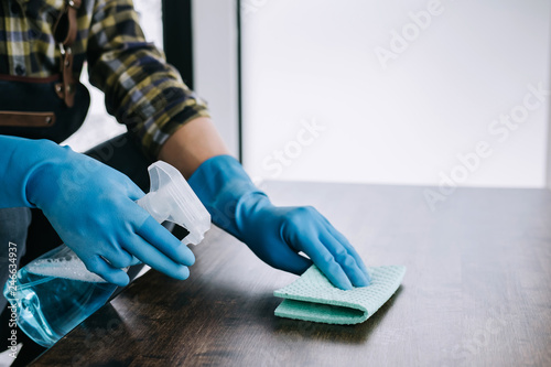 Husband housekeeping and cleaning concept, Happy young man wiping dust using a spray and a duster while cleaning on table at home