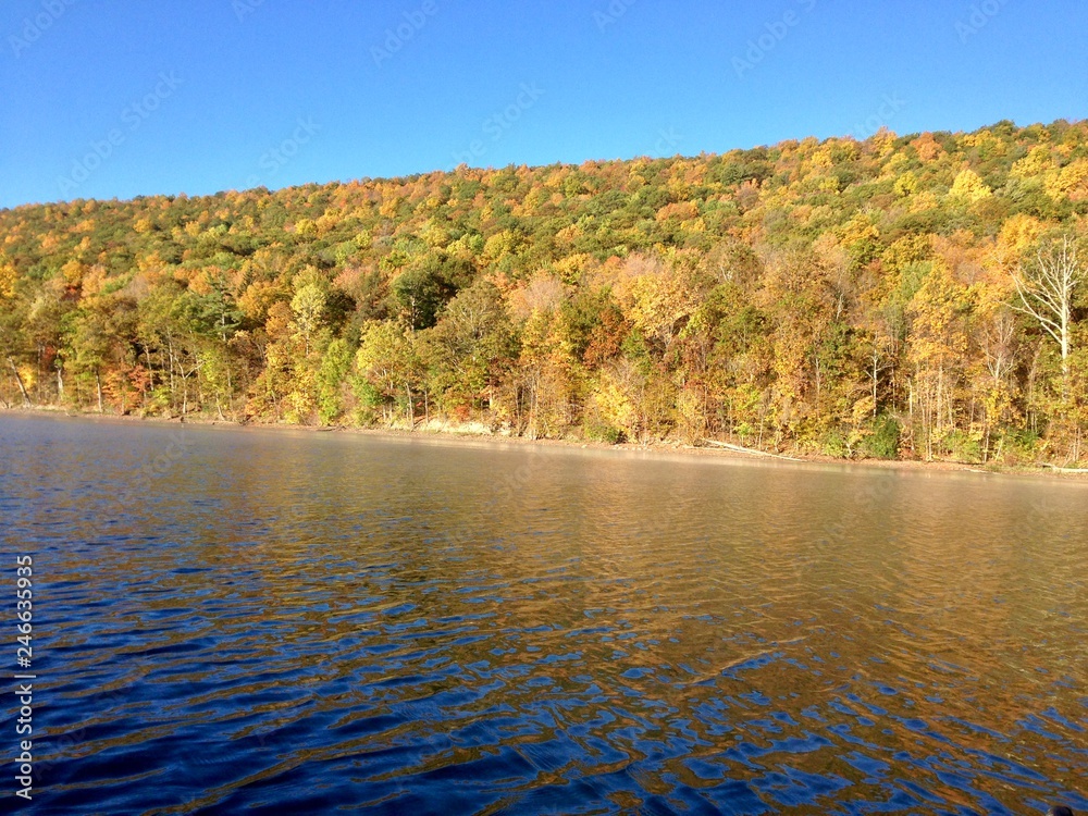 The clear, still water of Canadice Lake, one of Finger Lakes in New York, in horizontal orientation in Autumn, with a blue sky background 