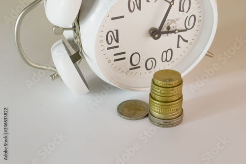 A stack of yellow euro coins, stands next to a white alarm clock close-up shot