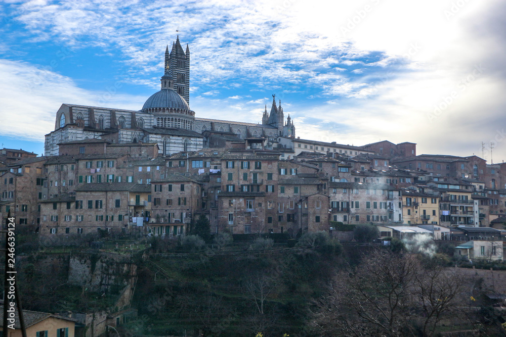 Panorama of Siena old town and cathedral with bell tower in winter morning with blue sky and clouds on the background, Tuscany, Italy