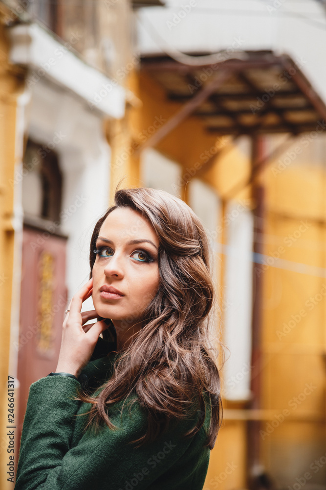 Close up portrait of fashionable romantic attractive young woman in green jacket at the small old city street