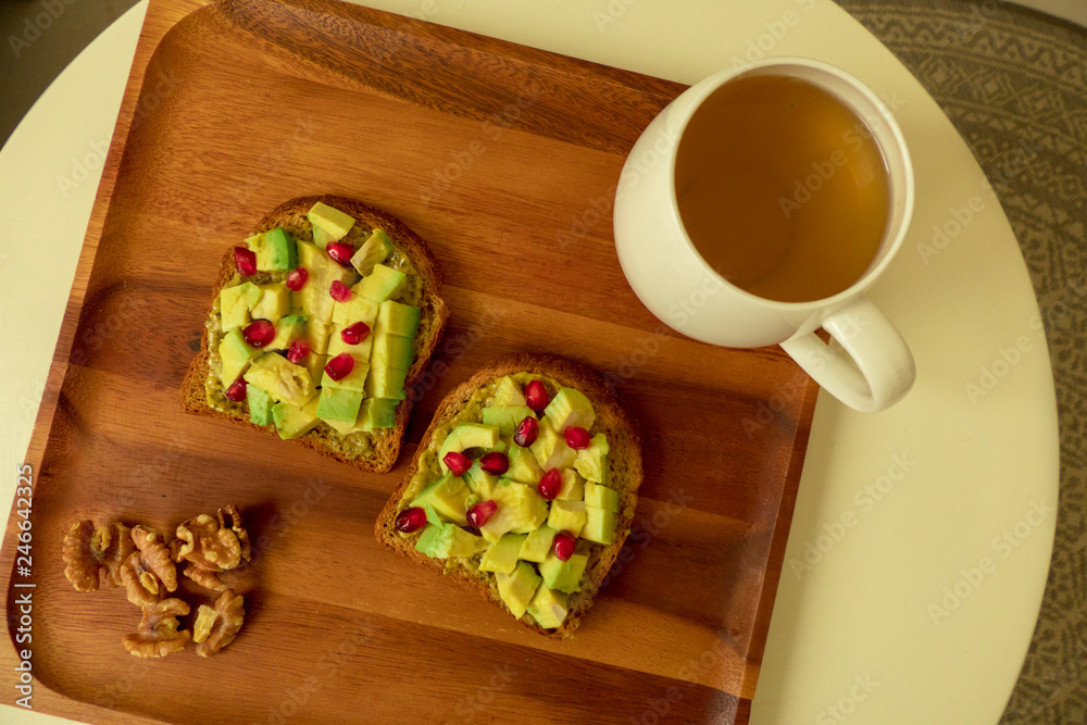 Two Avocado Toasts with pomegranate seeds on a wooden tray and a cup of tea