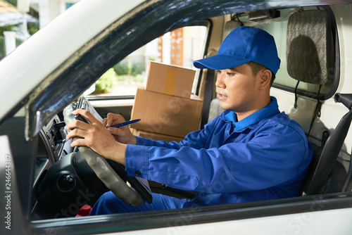 Young Vietnamese delivery man sitting in his van and filling document