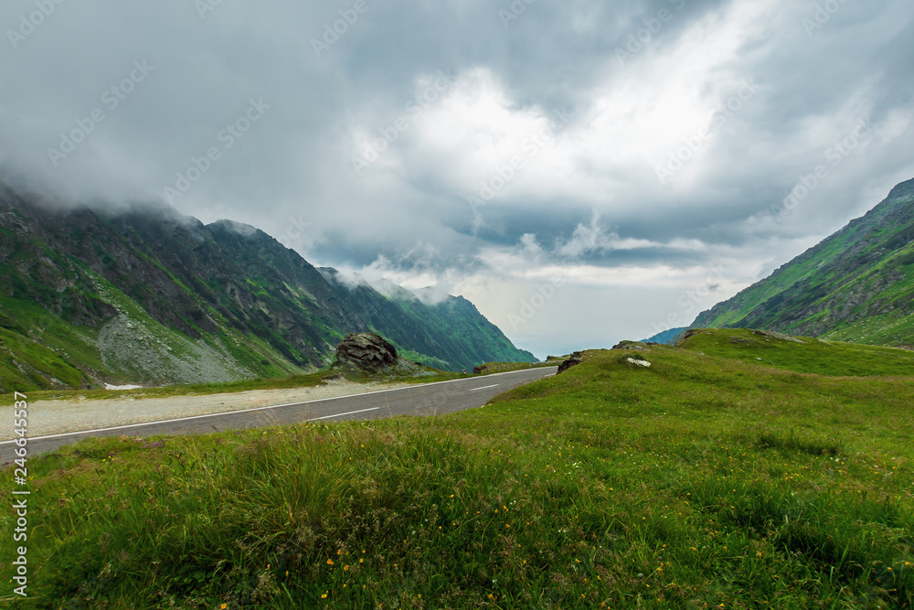 transfagarasan road in stormy weather. popular travel destination of romania. grassy meadow along on the edge of a hill. view in to the distant valley. overcast sky