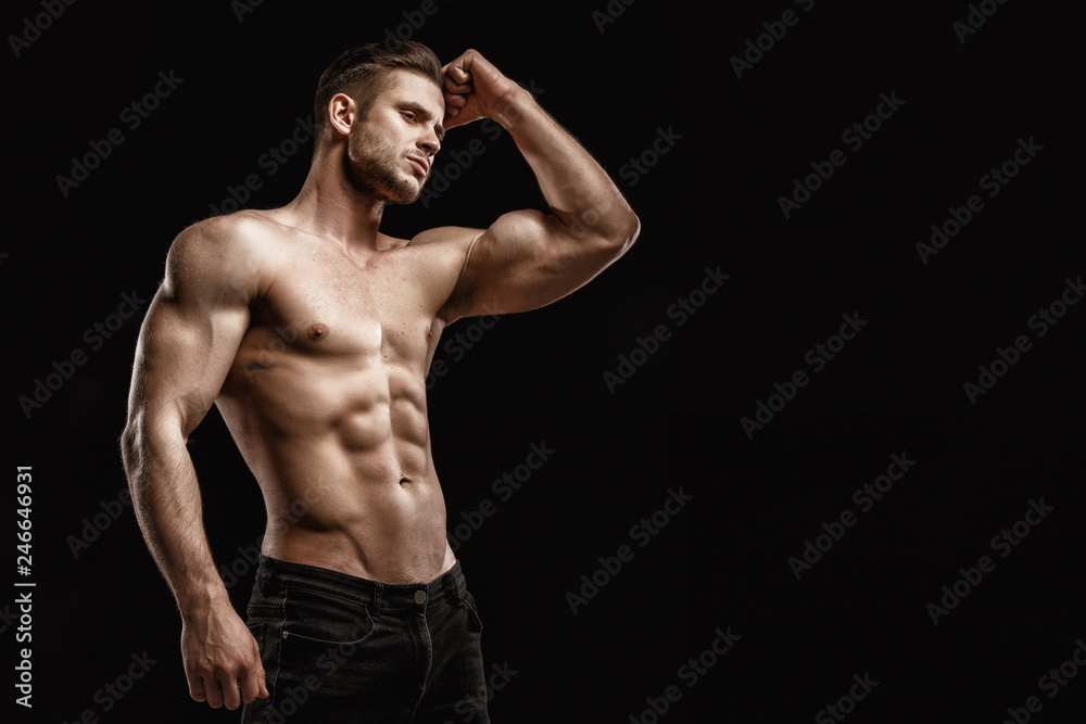 Muscular model young man on dark background. Fashion portrait of strong brutal guy with trendy hairstyle. Sexy naked torso, six pack abs. Male flexing his muscles. Sport workout bodybuilding concept.