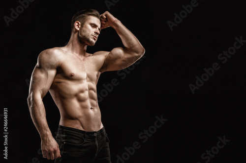 Muscular model young man on dark background. Fashion portrait of strong brutal guy with trendy hairstyle. Sexy naked torso, six pack abs. Male flexing his muscles. Sport workout bodybuilding concept. photo