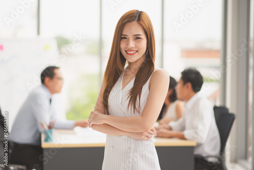 Successful business young Asian beautiful woman looking at camera while colleague discuss or meeting behind her in the office