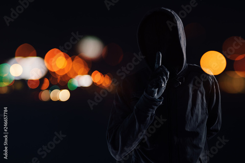 Hooded maniac with finger on lips gesturing shh sign photo