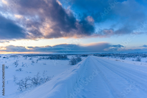 Winter Road covered in snow with tire tracks at sunset