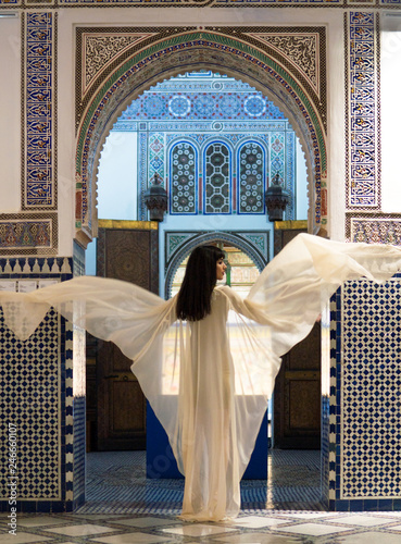 Beautiful Moroccan Girl Waving her white mantle in Rich interior of Picturesque Dar Si Said Riyad in Marrakech photo