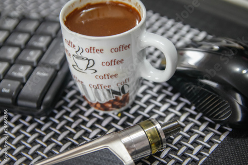 Electronic cigarette, cup of coffee, computer mouse and keyboard on table in living room