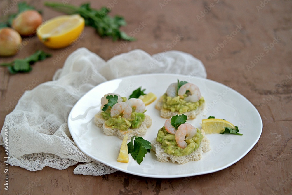 Small snack sandwiches on white bread with guacamole and shrimps on a white plate. Selective focus. Small snack sandwiches on white bread with guacamole and shrimps on a white plate. Selective focus.