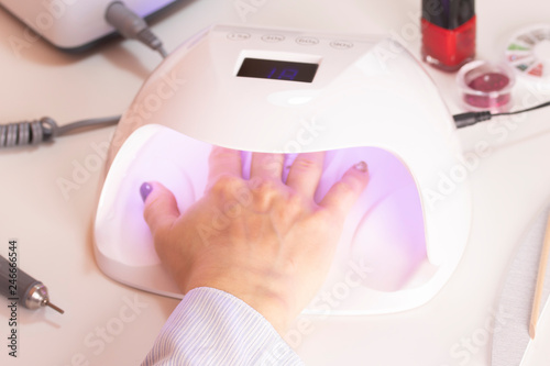 The hands of the girl in the UV lamp for nails on the manicure table