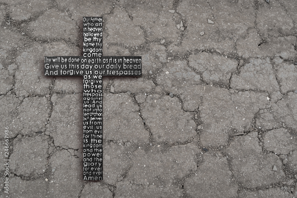 Wooden cross with the Lord's prayer on  black cracked ground, dry soil texture background