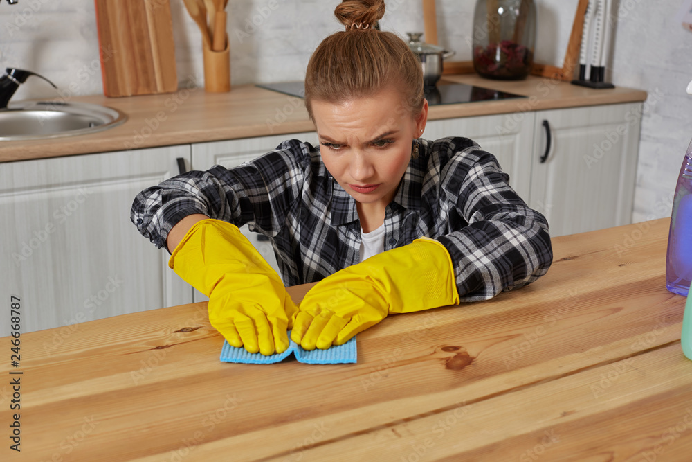 Young woman in protective gloves wipes a table in the kitchen with a rag Young woman in protective gloves wipes a table in the kitchen with a rag