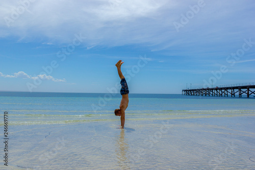 A Man doing a handstand on a Tropical White Sand Beach of Australia