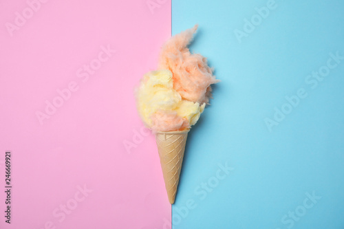 Ice cream cone with fluffy cotton candy on color background, top view