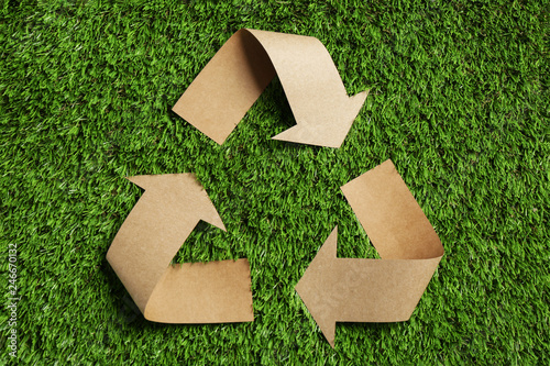 Recycling symbol cut out of kraft paper on green grass, top view