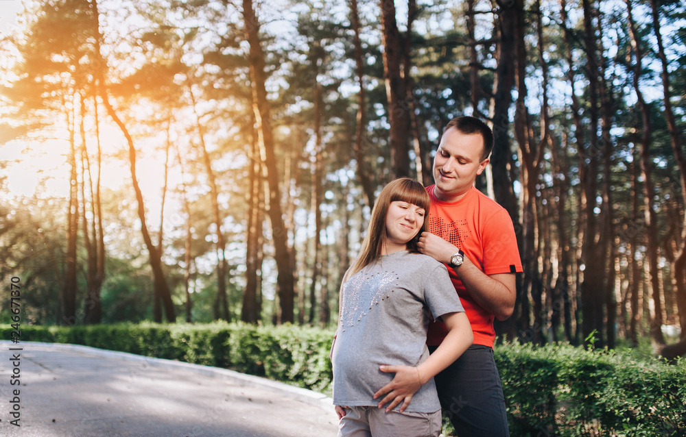 Fototapeta premium A stylish guy and a pregnant girl are standing in the forest and hugging. Pregnancy. Love of married people.