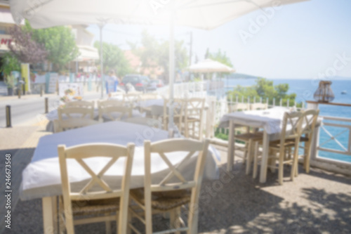 Restaurant tables and chairs below the sunshade on the terrace on the seashore. Blurred scene of the restaurant in Neos marmaras  Greece.