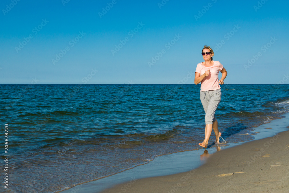 Fototapeta premium Middle-aged woman running on beach