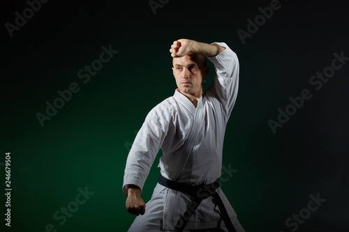 Adult athlete trains formal karate exercises on a dark green background