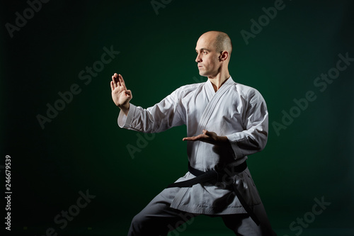Against the background of dark green athlete performs formal karate exercises