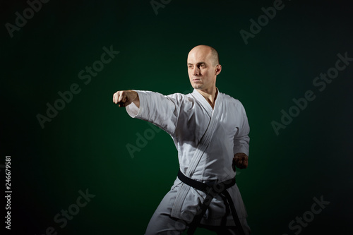Athlete doing formal karate exercises on a dark green background