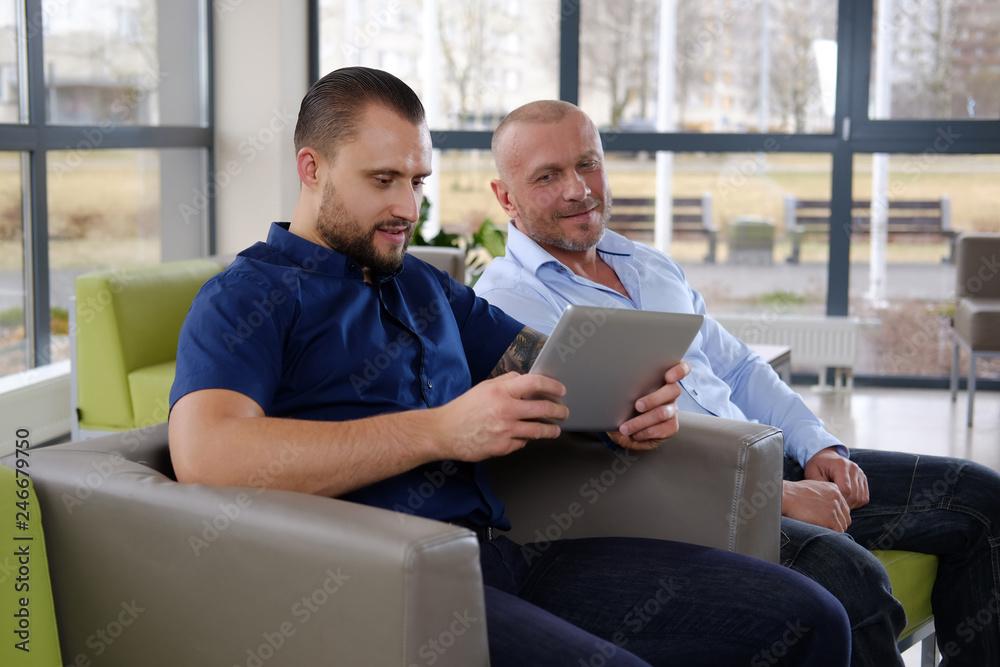 Fototapeta premium Coworkers are watching something funny in the tablet sitting on a couch in the office