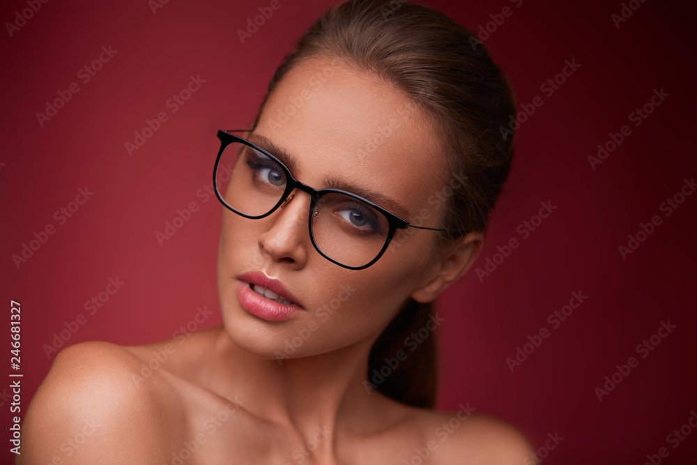 Attractive woman in square eyeglasses looking at camera on red background. Portrait of young beautiful blonde girl.Black frame spectacles.Vision correction,optical shop,glasses store,eyewear concept. Attractive woman in square eyeglasses looking at camera on red background. Portrait of young beautiful blonde girl.Black frame spectacles.Vision correction,optical shop,glasses store,eyewear concept.