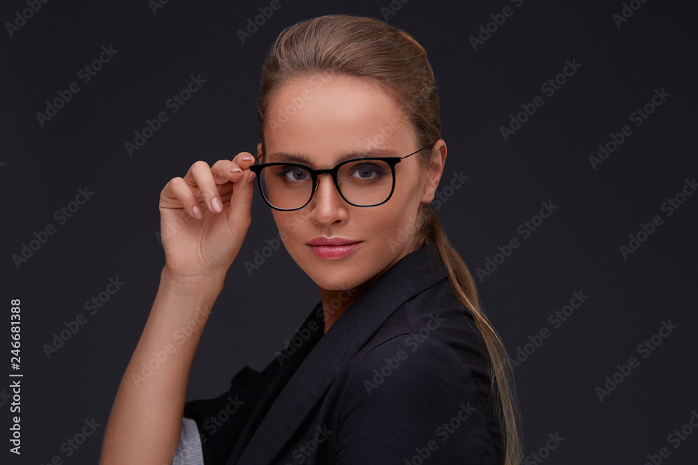 Elegant serious woman in square eyeglasses looking at camera on dark background.Adult beautiful businesswoman in jacket.Black frame spectacles.Vision correction,optical shop,glasses store concept. Elegant serious woman in square eyeglasses looking at camera on dark background.Adult beautiful businesswoman in jacket.Black frame spectacles.Vision correction,optical shop,glasses store concept.