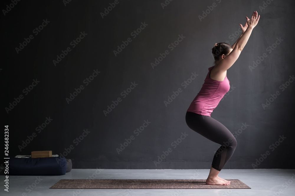 Woman practicing yoga, doing Chair exercise, Utkatasana pose, working out.