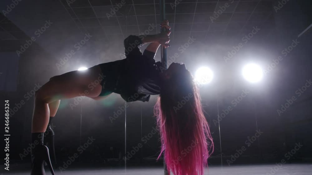 Dance and acrobatics concept. Sexy woman pole dancing in dark interior with lights and smoke