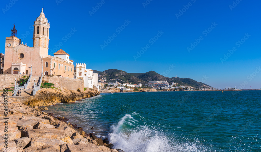 Sitges church with a blue sky Sant Bartomeu & Santa Tecla in Barcelona, Spain with the mediterranean sea and waves at the seawall